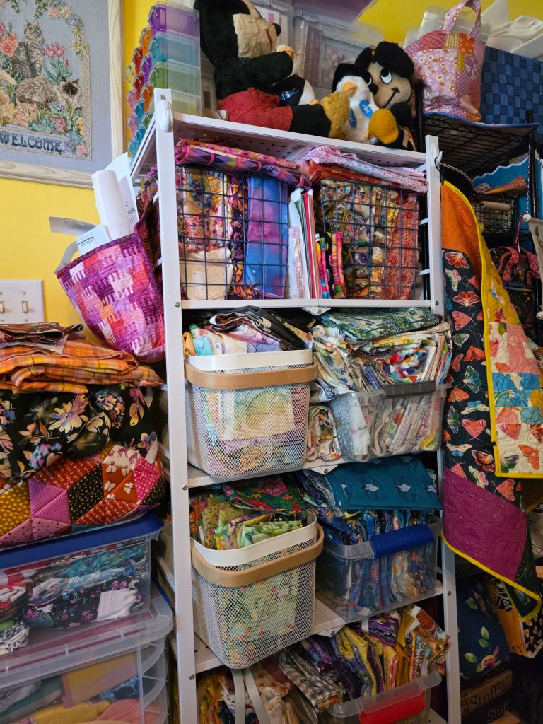 Colorful storage shelves filled with fabric baskets, quilting supplies, and stuffed animals in a craft room.