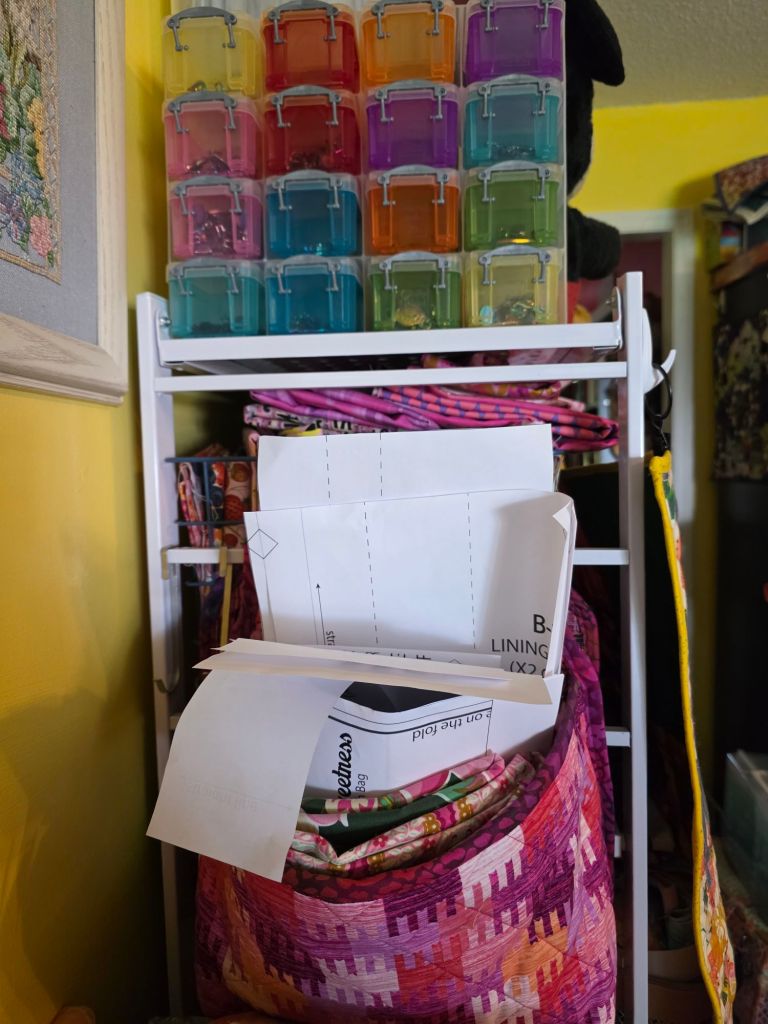 A shelf with colorful plastic storage bins stacked above and various craft materials, including sewing patterns and a quilt, stored below.