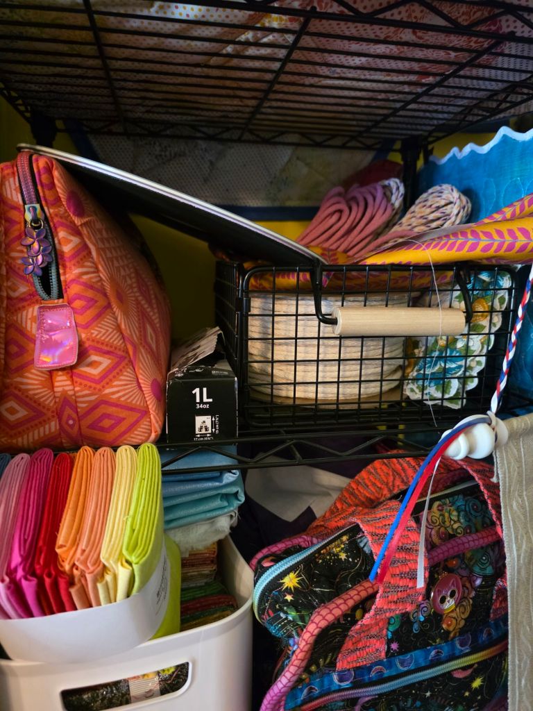Colorful storage items and fabrics displayed on a wire shelf, including various bags, a basket with a wooden rolling pin, and neatly folded linens.