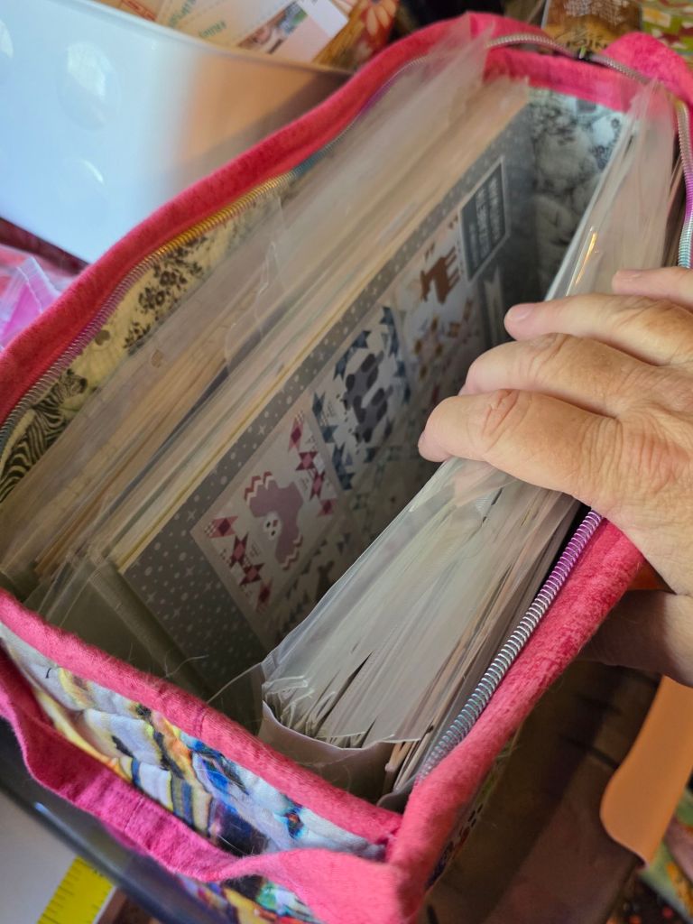 A close-up of a hand holding a colorful fabric bag filled with organized papers and scrapbook materials, showcasing various designs and textures.