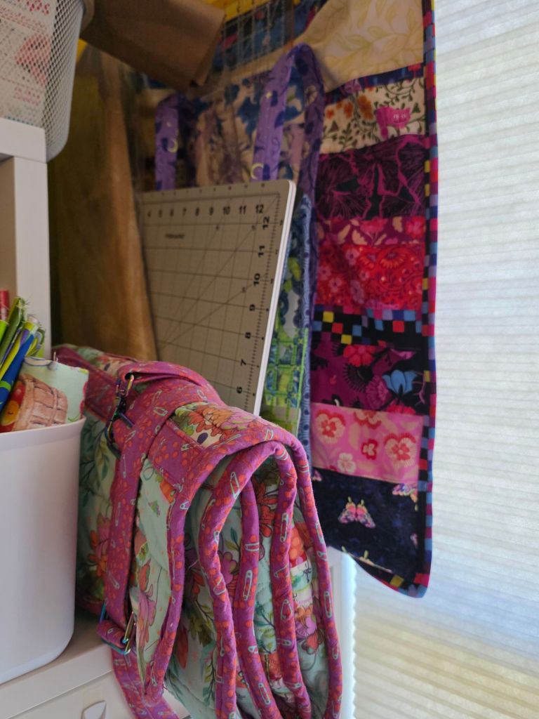 A view of a sewing space displaying folded colorful quilts, a cutting mat, and supplies in a basket.