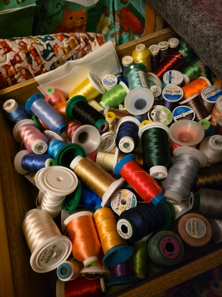 A wooden drawer overflowing with an assortment of colorful sewing threads and spools.