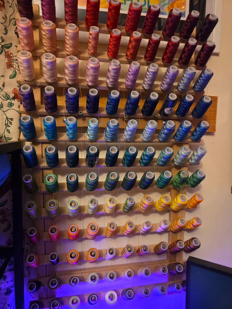 A colorful display of various spools of thread arranged on a wooden rack, featuring an array of colors including reds, blues, greens, and yellows.
