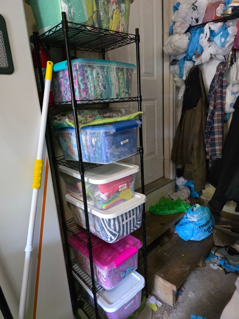 A metal shelving unit filled with colorful storage bins, organized by size, in a cluttered garage setting.