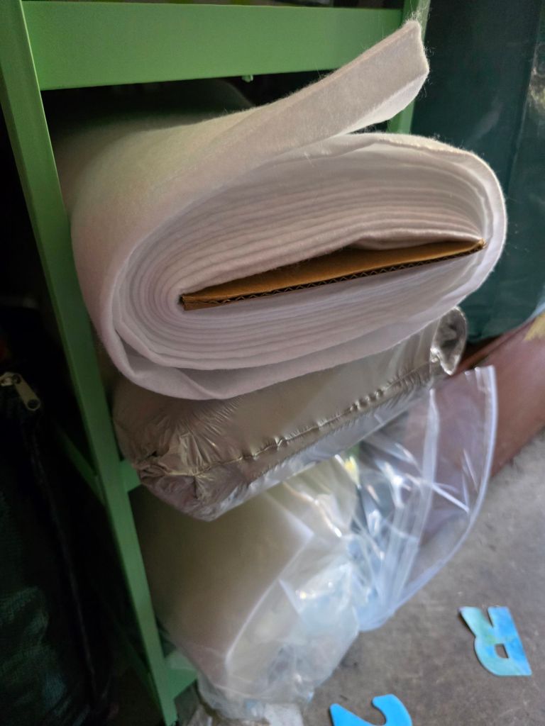Rolled white fabric stored on a green shelf, with additional packages of material beneath it.